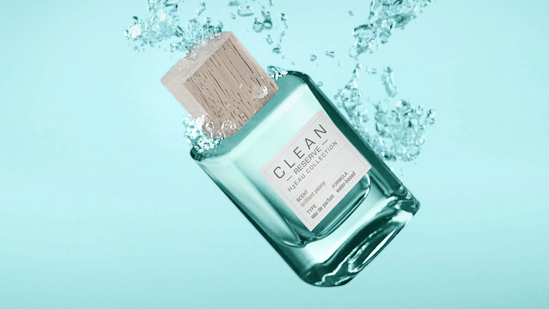 Flaska med Clean Reserve H2EAU Collection "Brilliant Peony" svävar i vatten mot en ljusblå bakgrund. Flaskan har en träliknande kork och genomskinlig design med en vit etikett som beskriver doften. 