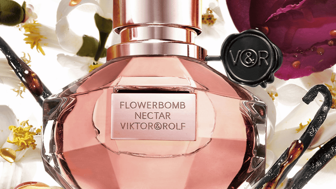 Bilden visar en närbild av Viktor & Rolfs parfym Flowerbomb Nectar. Flaskan är elegant och rosa med en svart sigilldetalj och omges av vaniljstänger och blommor, vilket framhäver den söta och blommiga karaktären hos doften.