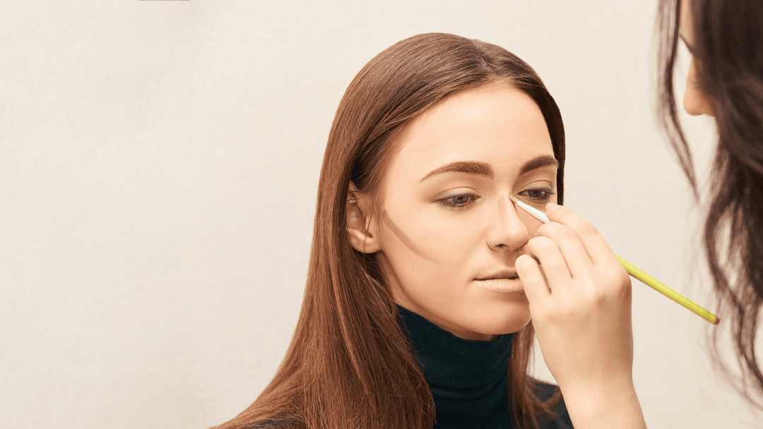 Makeupartist applicerar contouring på en kvinnas ansikte för att framhäva ansiktsdrag och skapa en skulpterad look. Mjuka linjer längs kindben och näsa visar tekniken för att definiera ansiktsformen.