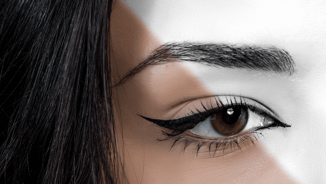 Närbild på ett öga med perfekt applicerad eyeliner och väldefinierade ögonbryn. Bilden är kreativt redigerad i färg och svartvitt, vilket framhäver ögonmakeupens precision och skönhet.