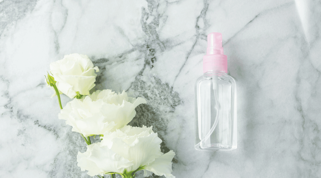 Tom body mist-flaska med rosa spraykork bredvid vita blommor på marmorbakgrund.